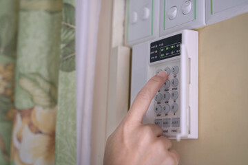 Woman entering code pin on home alarm system keypad. Close up shot. Home security concept.