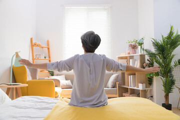 Senior Asia woman is sitting on the bed and stretch oneself in the morning at home