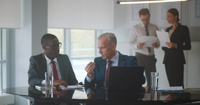 Secretary bring coffee to diverse business partners discussing contract on laptop