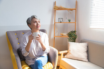 Senior woman holding a cup of coffee or tea relaxing at home in the morning.
