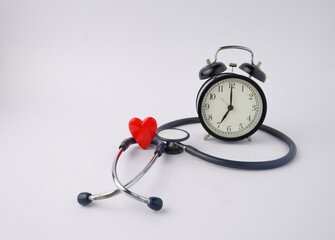 black alarm clock with medical stethoscope and red heart isolated on white background