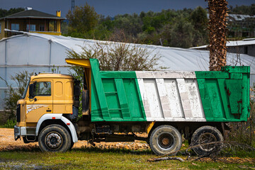 Dump truck with the image of the national flag of Nigeria is parked against the background of the countryside. The concept of export-import, transportation, national delivery of goods