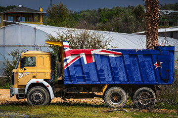 Dump truck with the image of the national flag of New Zealand is parked against the background of the countryside. The concept of export-import, transportation, national delivery of goods