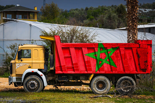 Dump truck with the image of the national flag of Morocco is parked against the background of the countryside. The concept of export-import, transportation, national delivery of goods