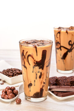 Iced Mocha Coffee Accompanied By Chocolate Pearls, Vegan Muffins And A Couple Of Chocolate Bars On A White Marble Surface And A White Background, Copy Space For Advertising, Fancy Concept.