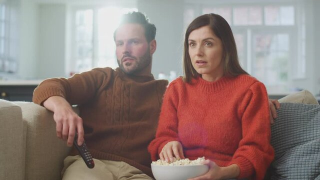 Couple sitting on sofa spilling popcorn ss they watch thriller on TV together - shot in slow motion