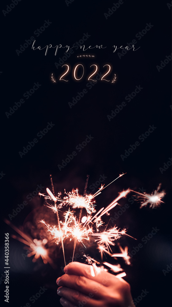 Poster make a wish new year 2022 with hand holding burning sparkler firework blast with on a black bokeh ba