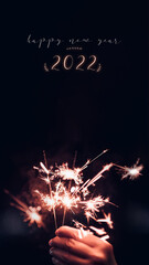 Make a wish new year 2022 with hand holding burning Sparkler firework blast with on a black bokeh...