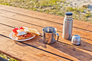 Breakfast in nature. Fried sandwich with egg, bacon, tomatoes and hot coffee from a thermos