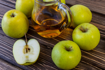 Green apples and jug with apple juice on wooden background