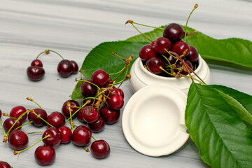 a cup of cherries and cherry leaves on a white painted wooden table