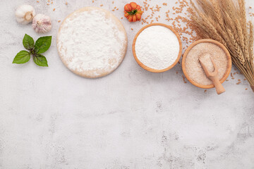 The ingredients for homemade pizza dough with wheat ears ,wheat flour and wheat grains set up on white concrete background.