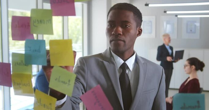 Smiling african american male employee write on colorful sticky notes develop business project in office
