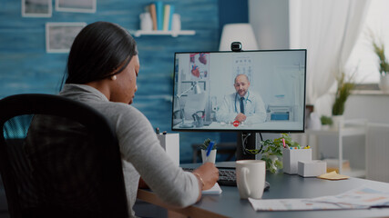 African american woman writing respiratory sickness treatment on notebook discussing pills treatment during online healthcare videocall meeting conference. Therapist doctor working remote from home