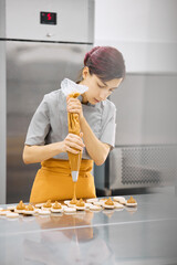 Pastry chef girl prepares fresh cakes at her small production facility