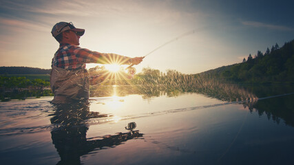 Fly fisherman stands in the water and casts the fly with fishing rod using Roll Cast with lot of...