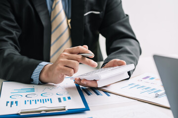 Close-up of a businessman hand holding a pen with a document calculator graph sheet placed at the office.