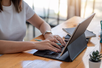 Close-up of a woman hand holding a pencil while using a tablet keyboard to work at the office.