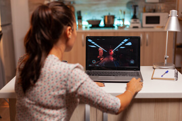 Lady playing games on laptop during night time during night time in home kitchen. Professional...