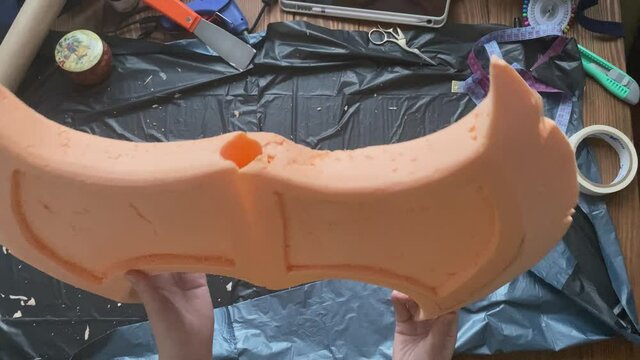 Woman makes viking hatchet for cosplay festival. Hands try on handle of pipe to axe made of styrofoam. Crafter's workshop. Garbage bag is on table.