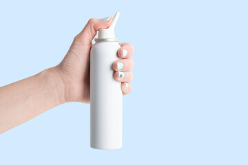 spray bottle with salt sea water for nasal cavity hygiene in female hand isolated on blue background