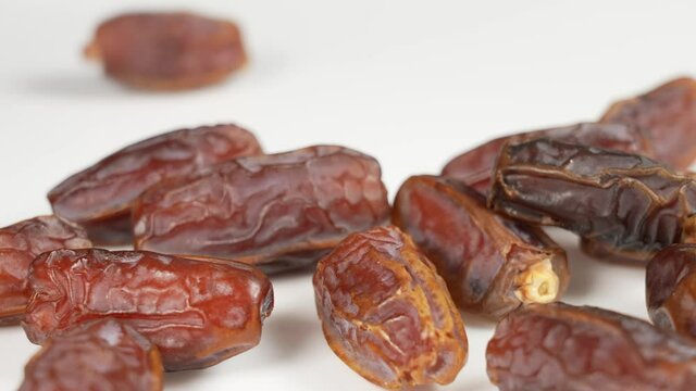 Close up view 4K stock video footage of tasty brown dried dates fruits falling down slowly on white background