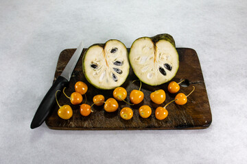 Chirimoya y Uchuva -Aguaymanto - Uvilla, an exotic Peruvian-Latin American fruit, sits on a brown wooden board, next to a kitchen knife.