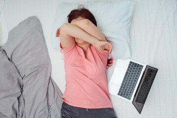 Naklejka premium Woman tired after working in a laptop covered her face with her hands and fell asleep lying in bed
