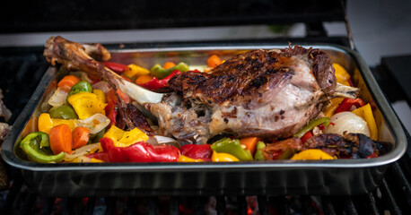 Cooking a delicious leg of lamb on a BBQ with peppers and potatoes in metal tray