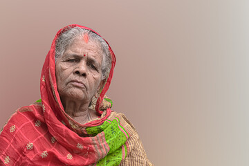 Beautiful portrait of elderly woman from India, having wrinkles on face and white grey hair, wearing colorful ethnic red saree with veil and is thoughtful. Plane background for tagline or advertising.