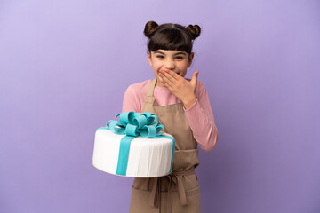 Pastry little girl holding a big cake isolated on purple background happy and smiling covering mouth with hand