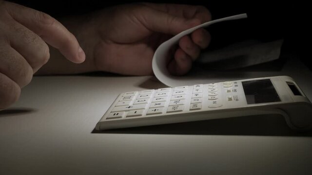 Businessman Working Late, with Invoices, Makes Financial Calculations with Adding Machine. Accounting Fee and Taxes Calculations.