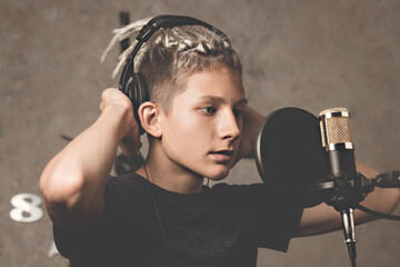 Stylish attractive guy with dreadlocks is recording a song in the studio. A young singer in black studio headphones stands in front of a microphone. Generation Z young talent