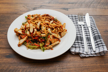Simple chicken chow mein meal on a white plate and on a wooden table. Chinese style tasty noodles with sauce and vegetables