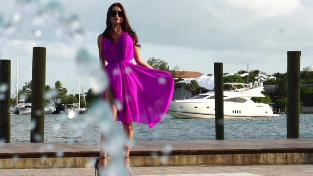 Slow motion on sexy young woman in purple dress walking by the dock and pool