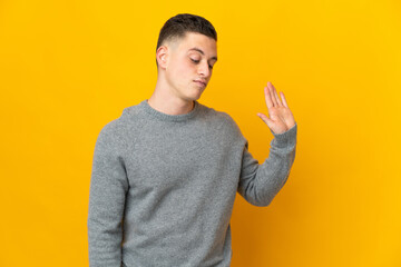 Young caucasian man isolated on yellow background making stop gesture and disappointed