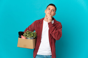 Young caucasian man making a move while picking up a box full of things isolated on blue background...