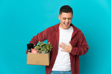 Young caucasian man making a move while picking up a box full of things isolated on blue background...