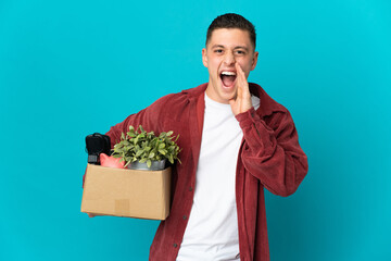 Young caucasian man making a move while picking up a box full of things isolated on blue background...