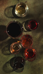 Red, rose and white wine in glasses on rusty green background, top view. Wine bar, shop, winery, wine tasting concept. Hard light and harsh shadows