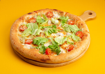 Pizza with tomatoes and salad on a yellow background.