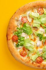 Pizza with tomatoes and salad on a yellow background.