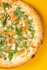 Pizza with cheese and arugula on a yellow background.