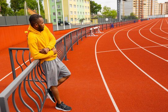 Handsome African American runner athlete in yellow sportswear having a break, doing running training, preparing for important competition at stadium . Healthy sport lifestyle concept