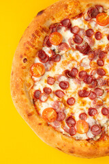 Pizza with sausages and tomatoes. On a yellow background.