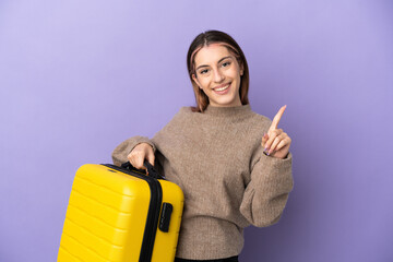 Young caucasian woman isolated on purple background in vacation with travel suitcase and counting...