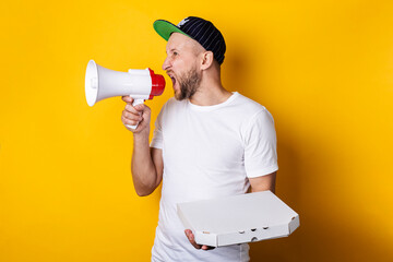 Young man shouting into a megaphone holding packed pizza on a yellow background