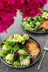 Peonies in a vase and dinner on the table, a plate of fried pork steak and a mix salad with cauliflower and avocado