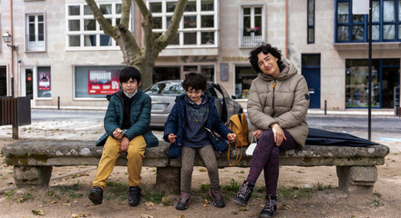 Fototapeta na wymiar young mother sitting with hers two sons of hers on a stone bench in an urban park
