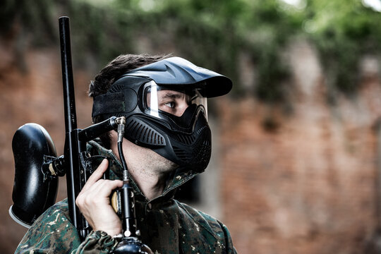 Portrait of young man with protective mask, paintball gun and camouflage wear, ready for an action paintball game